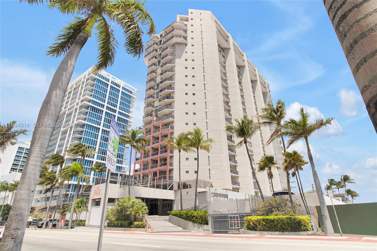 Condominium tower on Collins Avenue framed by palm trees and a neighboring high-rise.