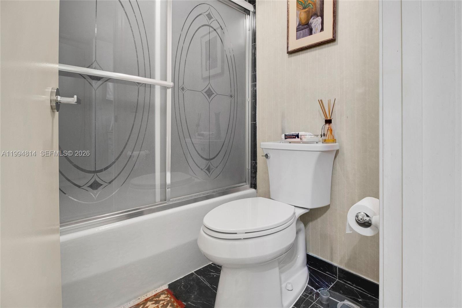 Bathroom with a white toilet, bathtub, and patterned frosted-glass shower doors.