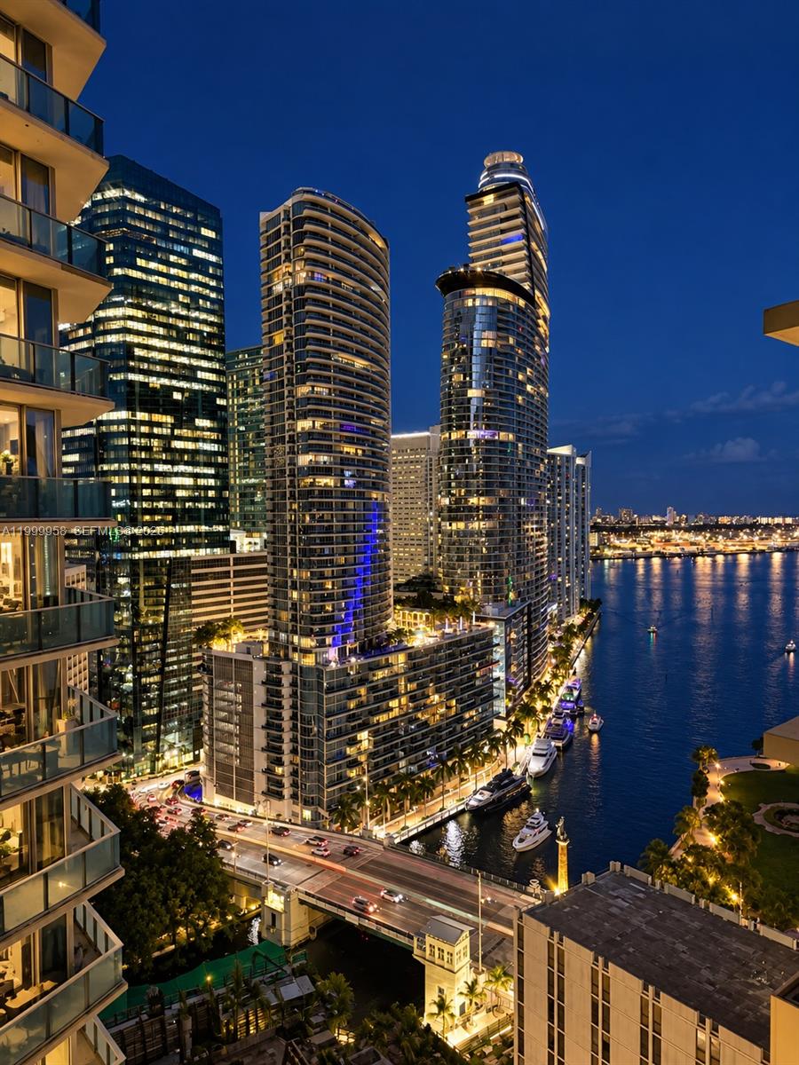 Downtown Miami skyline and waterfront at night, with illuminated towers, boats, and a bridge.