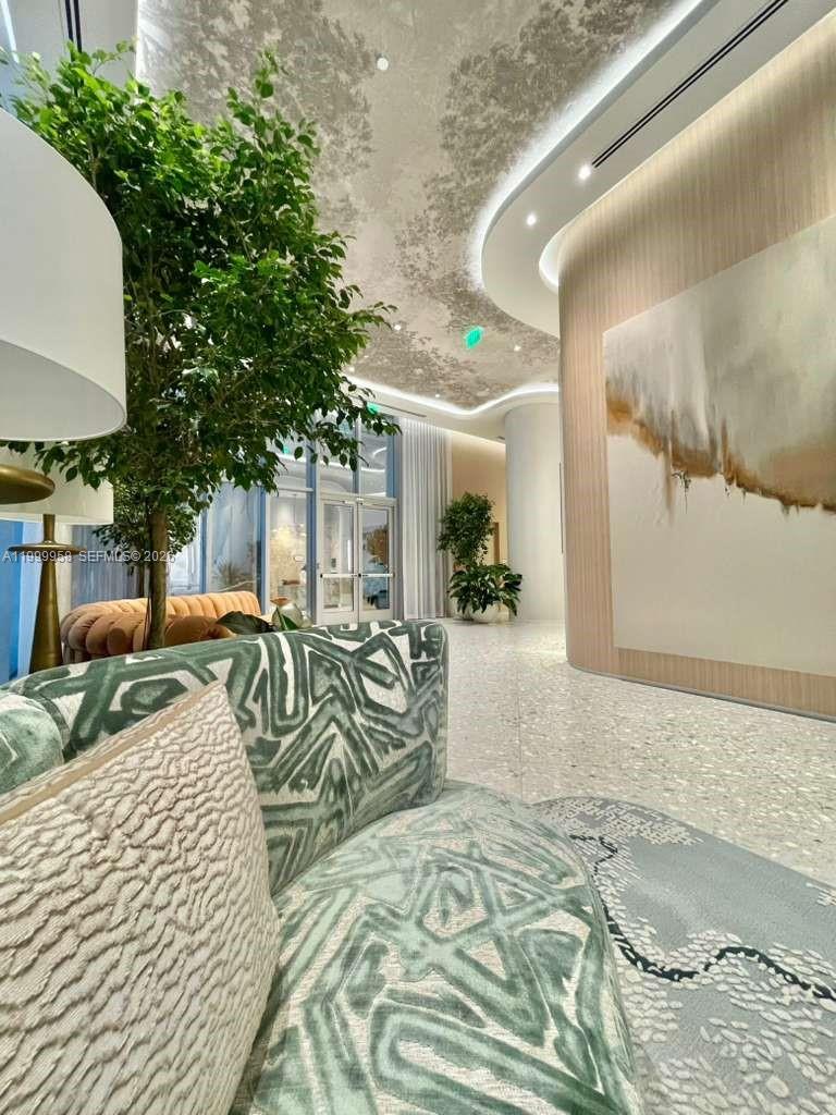 Condominium lobby with patterned green seating, a large indoor tree, and abstract art on a curved wall.