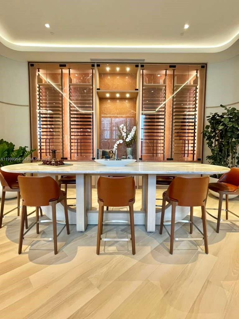 Dining area with a marble table, brown leather chairs, and illuminated built-in shelving.