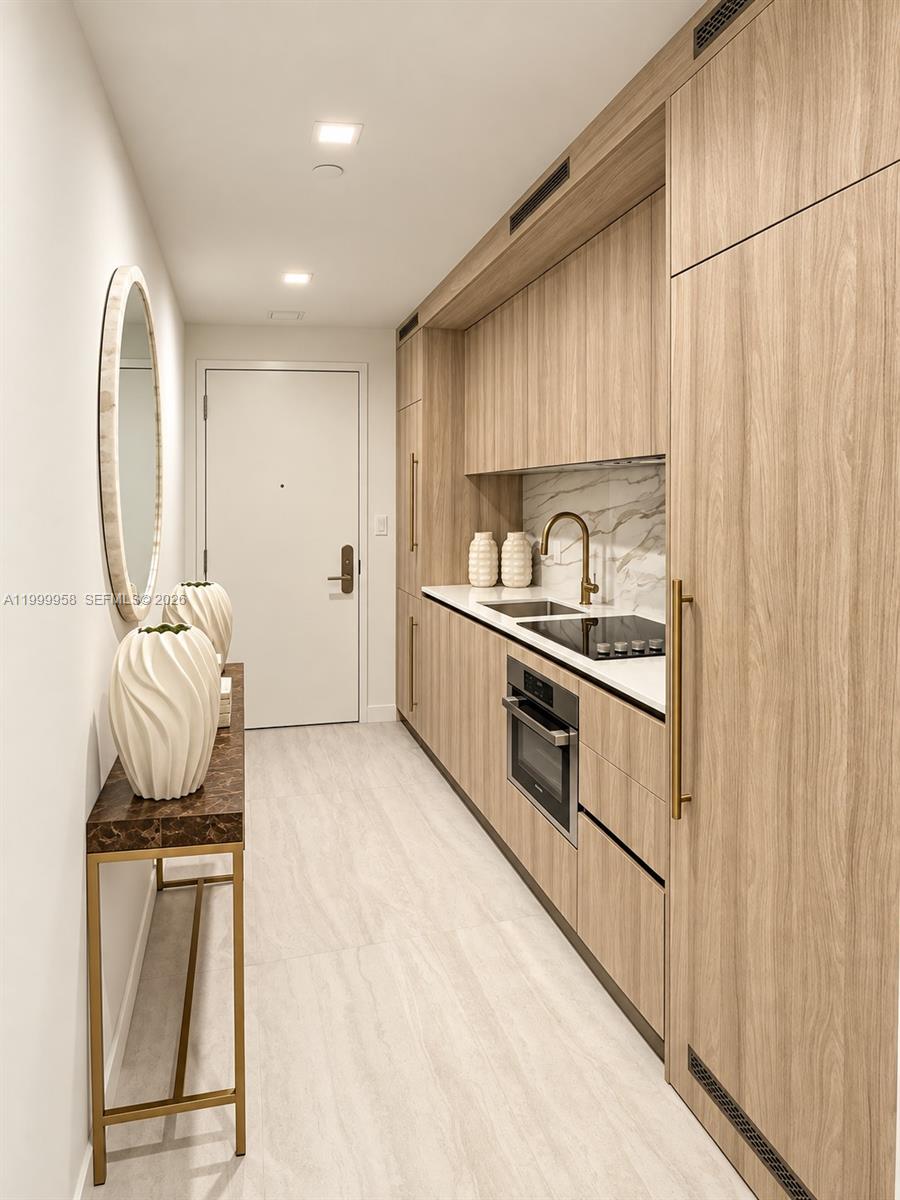Compact kitchen with light wood cabinetry, marble-look backsplash, and built-in appliances.