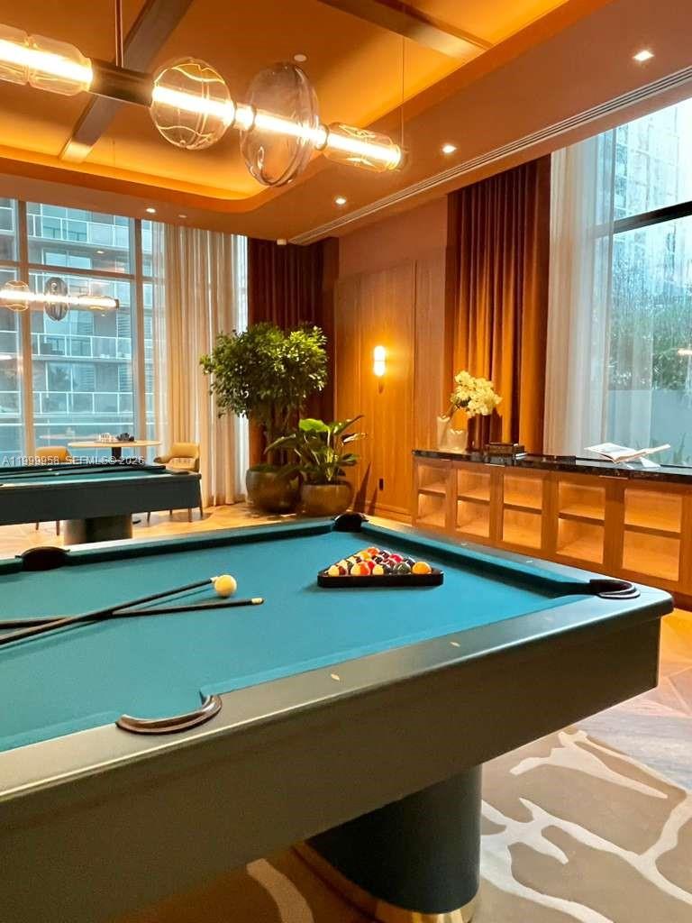Billiards room with a teal-felt pool table, pendant lights, and tall windows.
