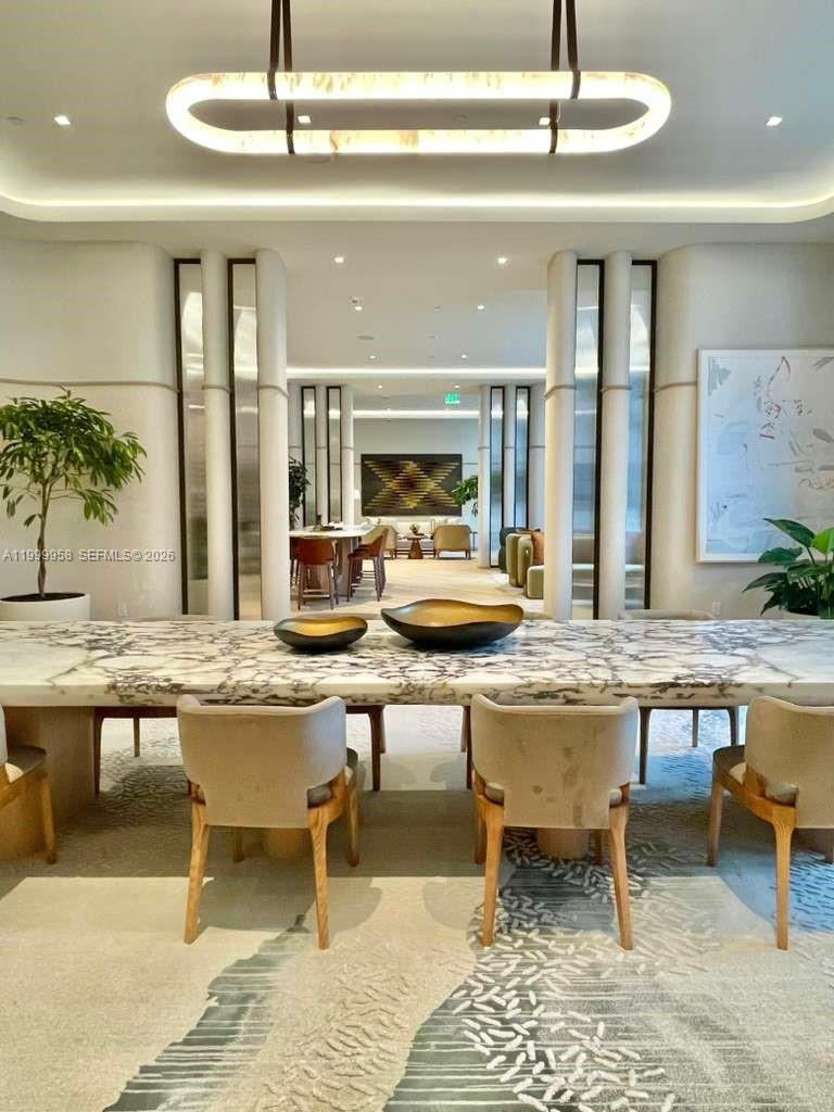 Furnished condo lounge with a marble dining table, upholstered chairs, and sculptural ceiling light.