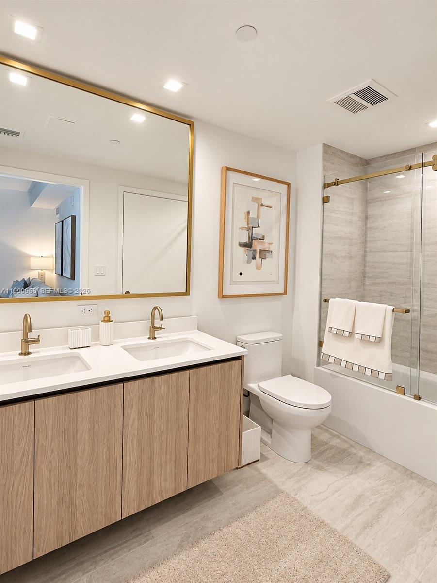 Modern bathroom with a double-sink wood vanity, gold-framed mirror, and glass-enclosed tiled shower.