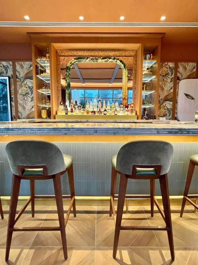 Bar area with a stone counter, mirrored shelving, bottles, and two upholstered wooden stools.