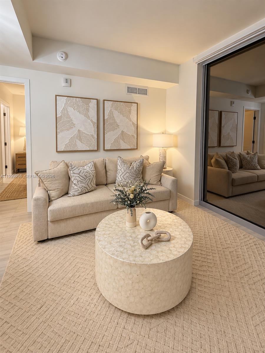 Staged living room with a beige sofa, botanical wall art, and a round coffee table on a woven rug.