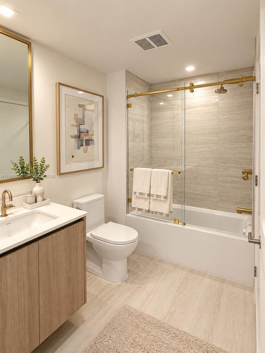 Bathroom with a wood vanity and tub-shower behind glass with gold hardware.