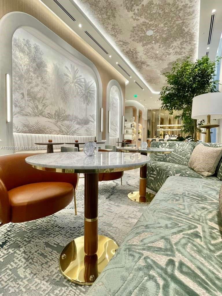 Furnished lounge with marble tables, patterned sofas, leather chairs, and large botanical wall murals.