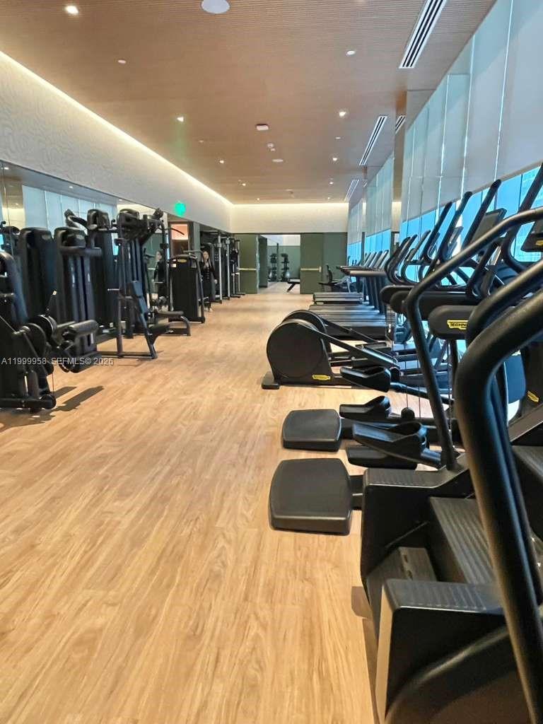 Fitness center with rows of treadmills beside floor-to-ceiling windows and weight machines.