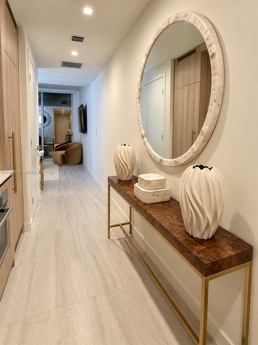 Staged condo hallway with an oversized oval mirror, sculptural vases, and a wood-and-gold console table.