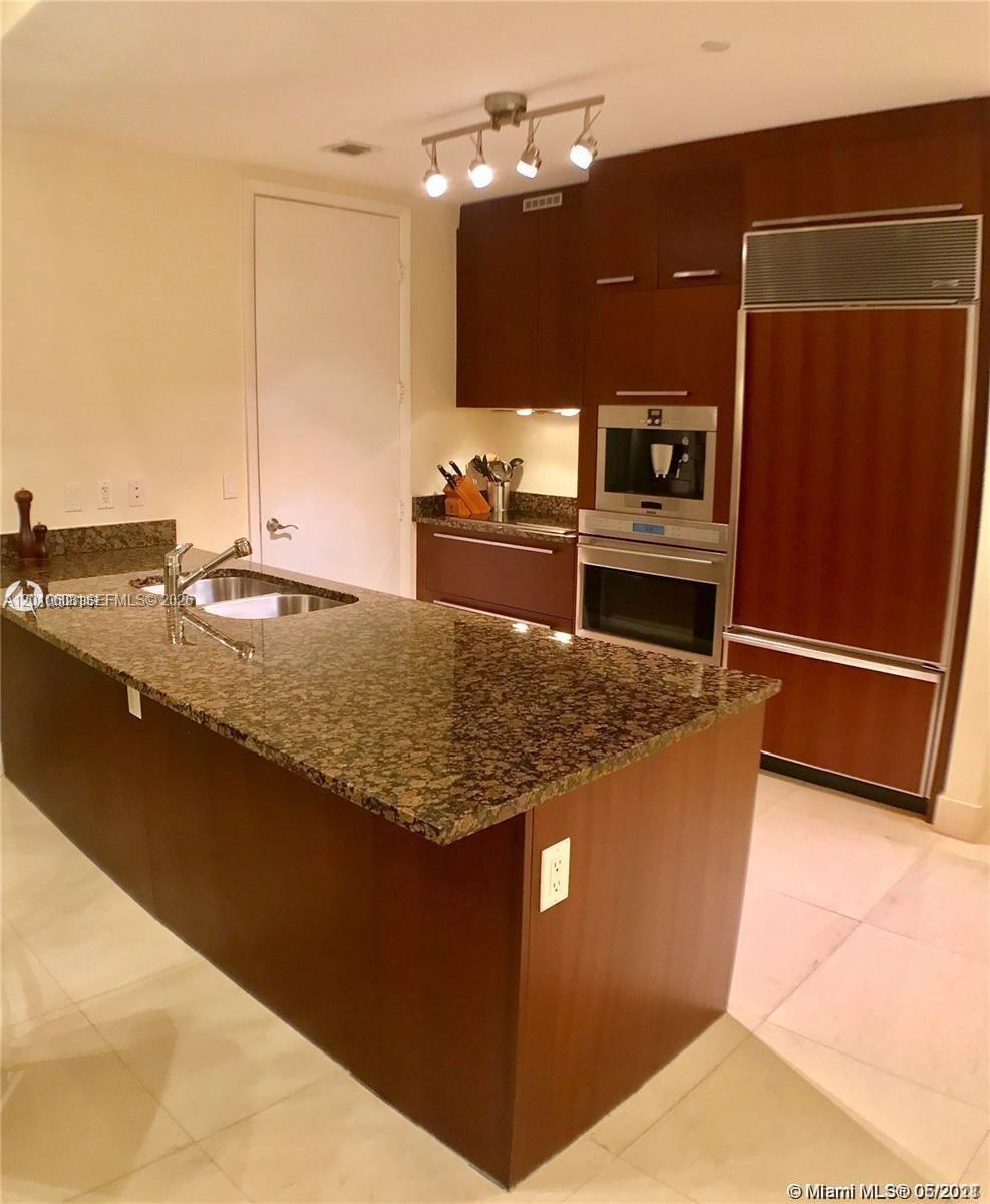 Condo kitchen with a large granite island, dark wood cabinets, and built-in appliances.