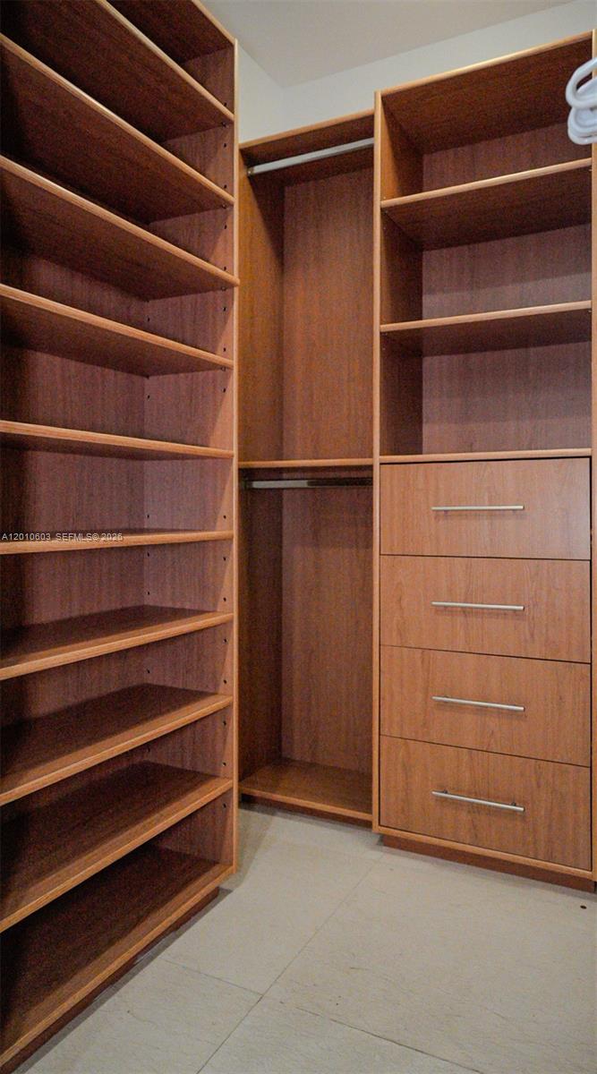 Walk-in closet with extensive wood shelving, built-in drawers, and hanging space.