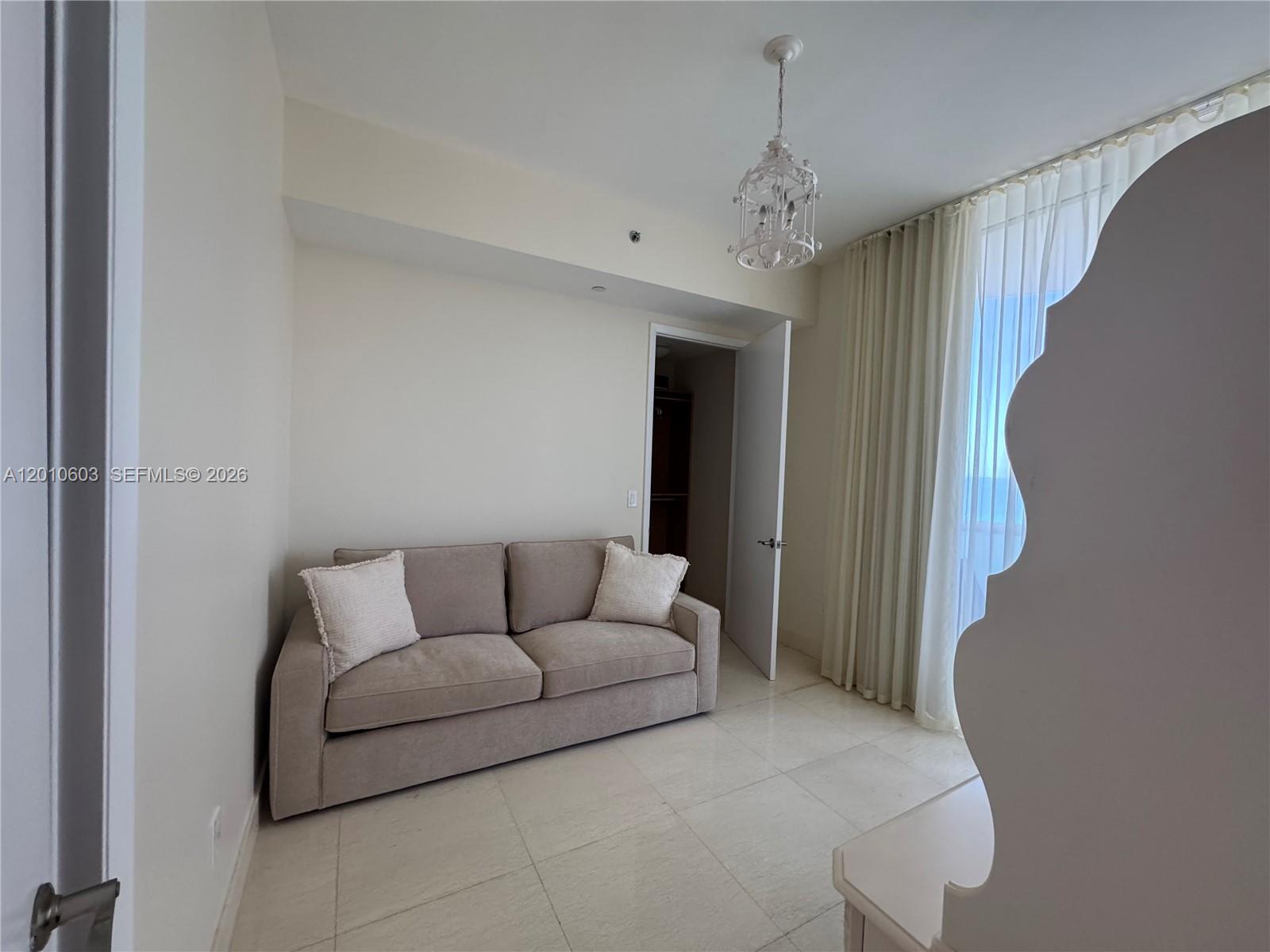 Furnished room with a beige sofa, floor-to-ceiling curtains, and a decorative chandelier.