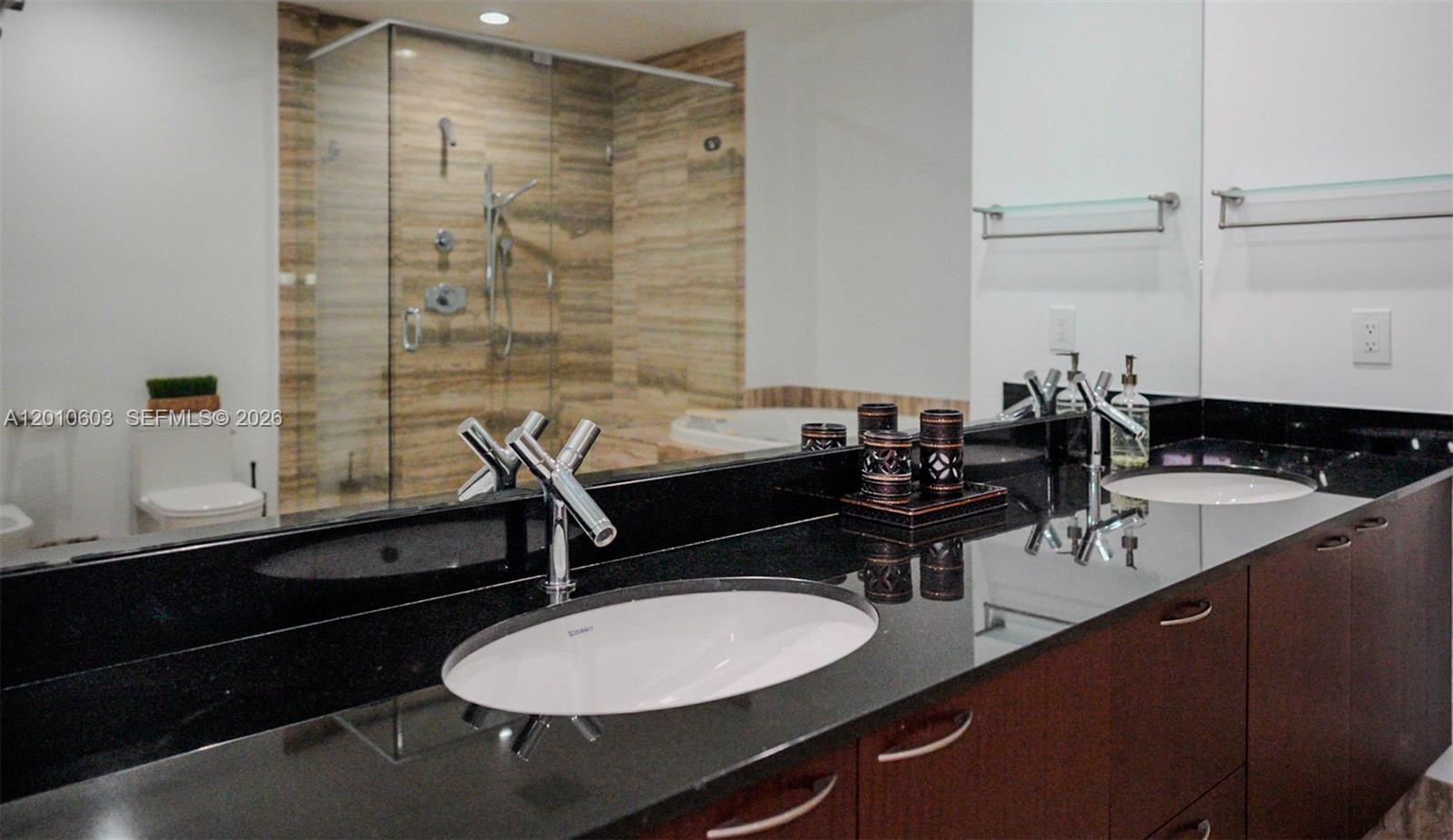 Bathroom vanity with black stone counters and a glass-enclosed tan stone shower.