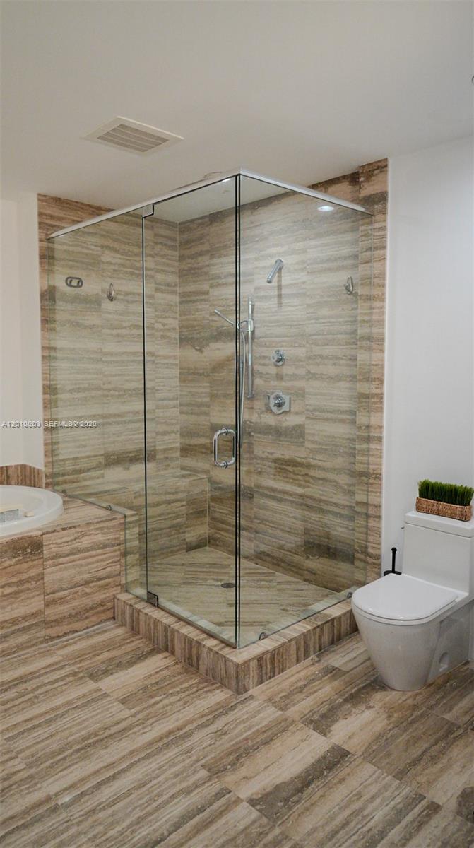 Bathroom with a glass-enclosed walk-in shower and beige-brown stone tile.