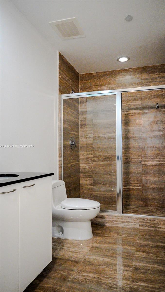 Bathroom with a glass shower, brown stone tile, white toilet, and vanity.