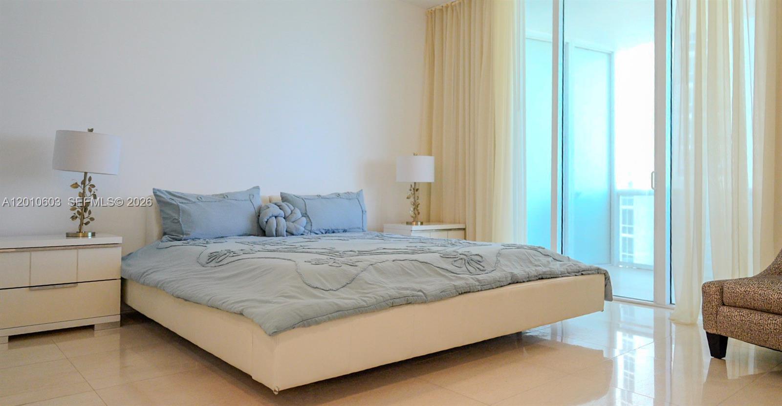 Furnished bedroom with a large pale blue bed beside sliding glass balcony doors.