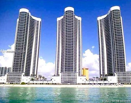 Three waterfront residential towers rise behind turquoise water under a blue sky.