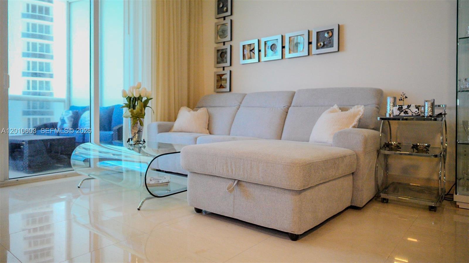 Living room with a pale sectional sofa and chaise beside floor-to-ceiling windows.