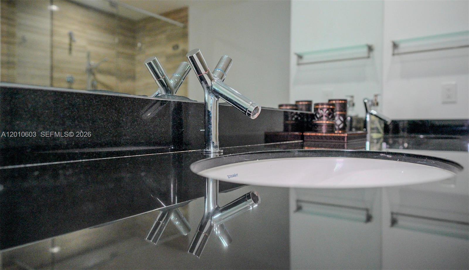 Bathroom sink with a chrome faucet on a glossy black granite vanity and mirrored backsplash.