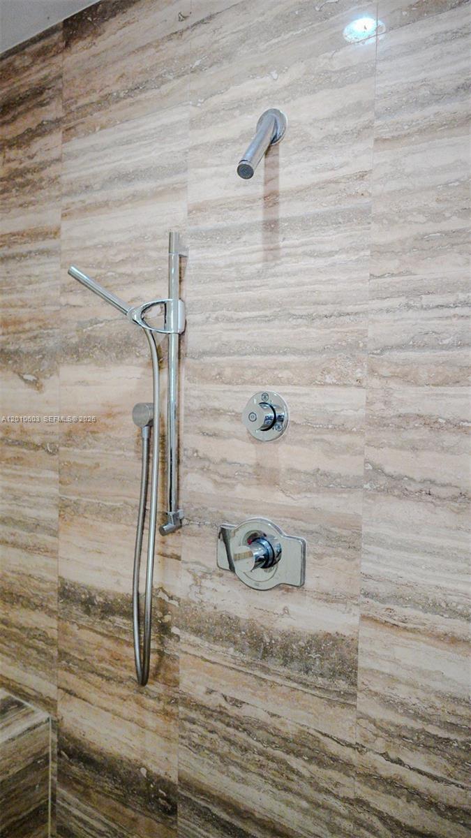 Stone-tiled shower with a chrome handheld wand and matching controls.