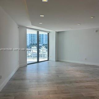 Empty room with light wood-look floors and sliding glass doors overlooking high-rise buildings.