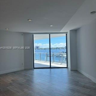 Unfurnished room with wood-look flooring and sliding glass doors opening onto a water-view balcony.