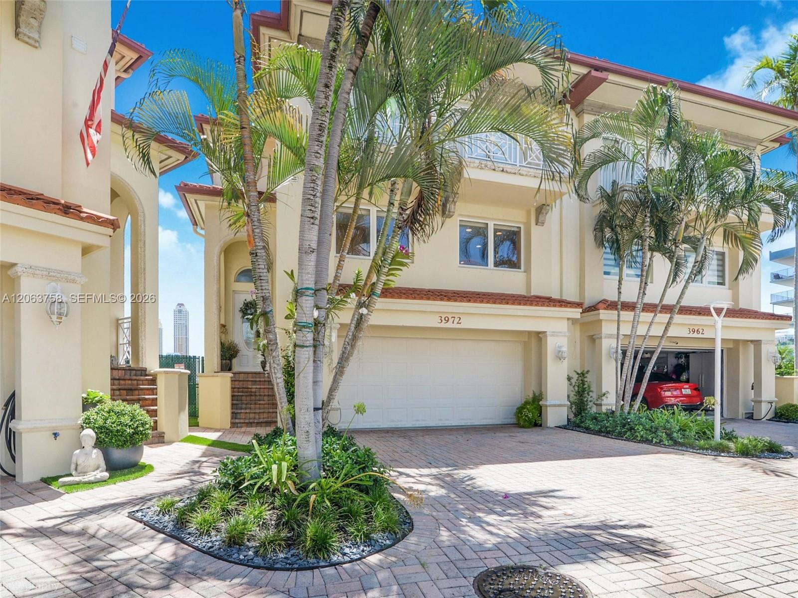 Cream two-story home with an arched entry, palm trees, and a brick-paver driveway.