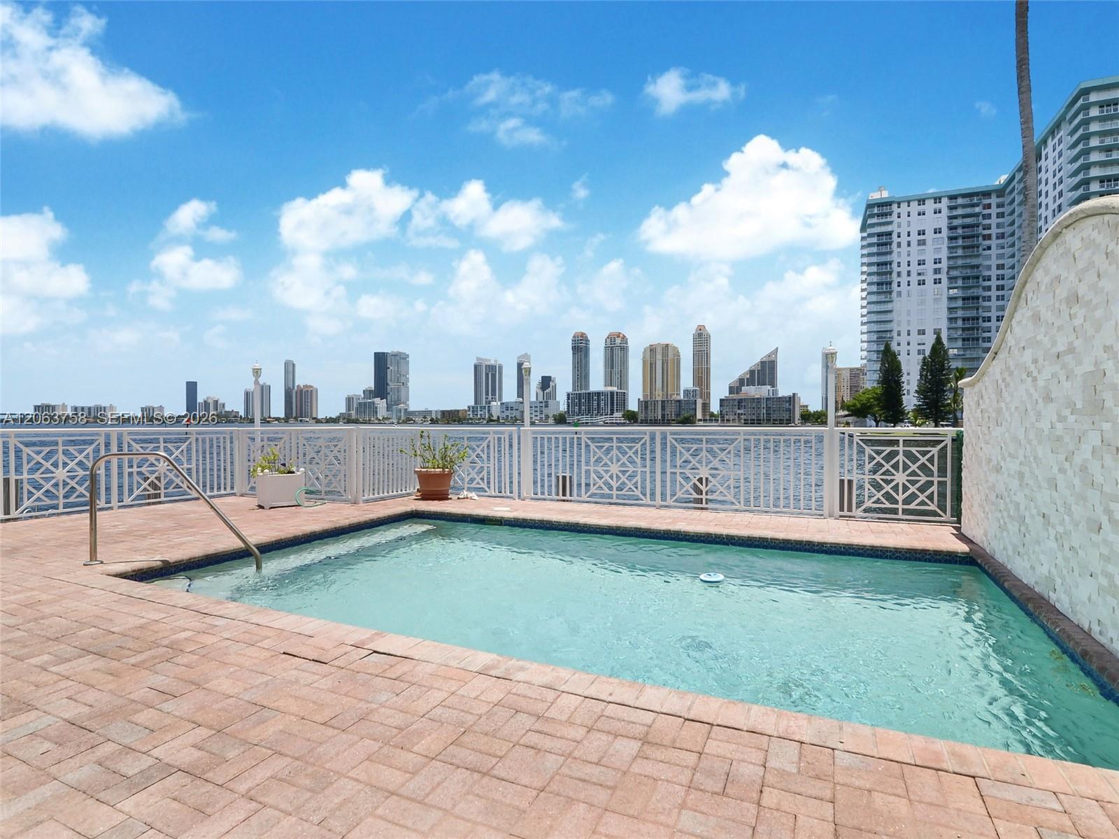 Waterfront swimming pool with a city skyline across the bay and a paved deck.