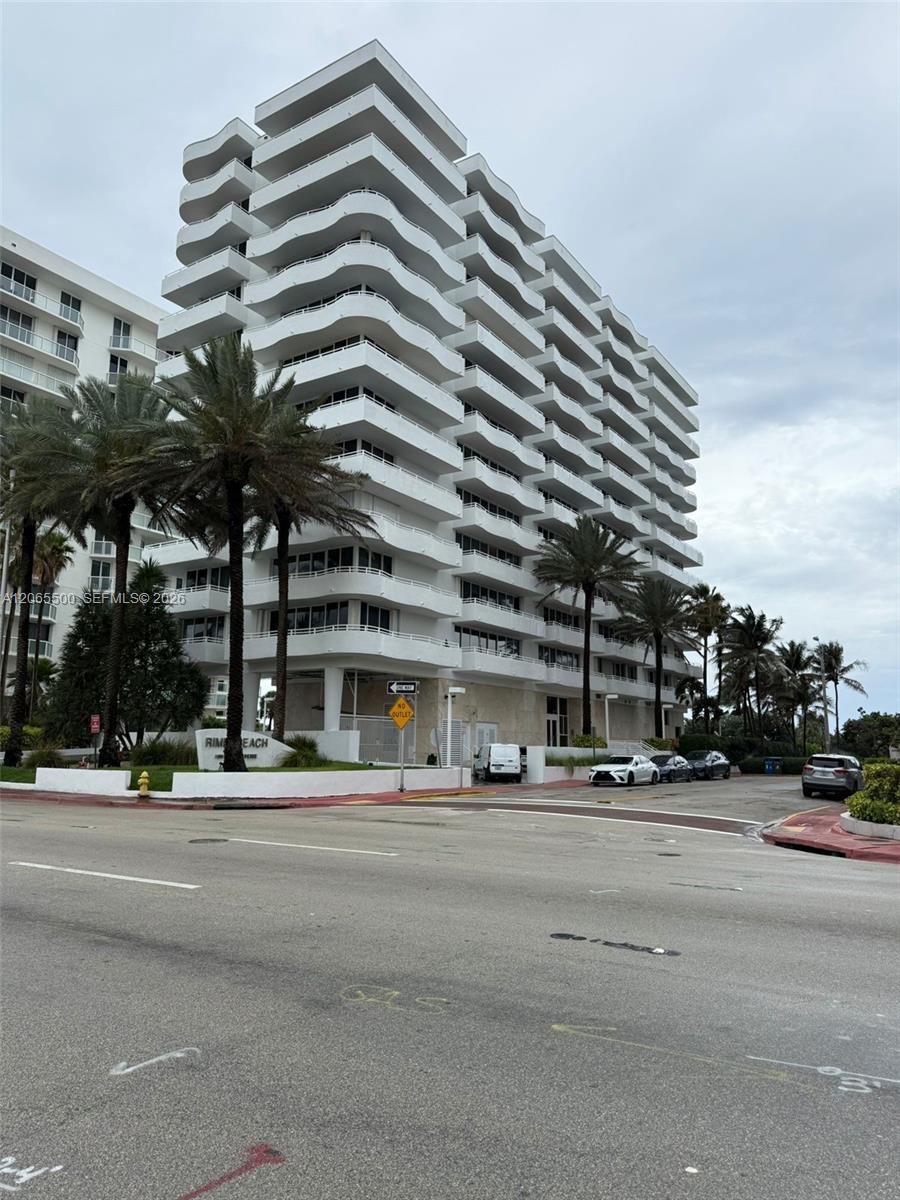 White condominium tower with curved balconies and palm trees along the street.