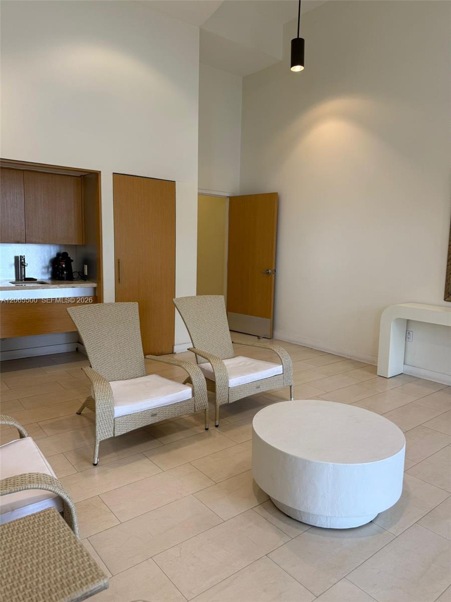 Furnished sitting area with woven chairs and a round white coffee table beside a kitchenette.