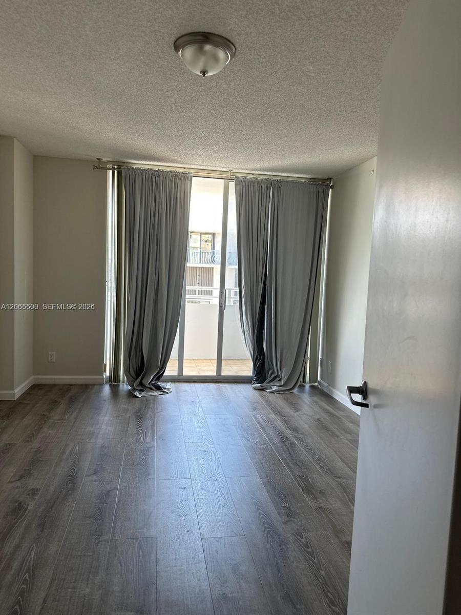 Empty room with gray wood-look flooring and curtained sliding glass doors opening to a balcony.