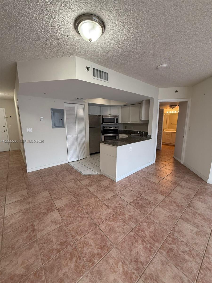 Vacant condo kitchen with white cabinets, stainless steel appliances, and a dark stone breakfast bar.