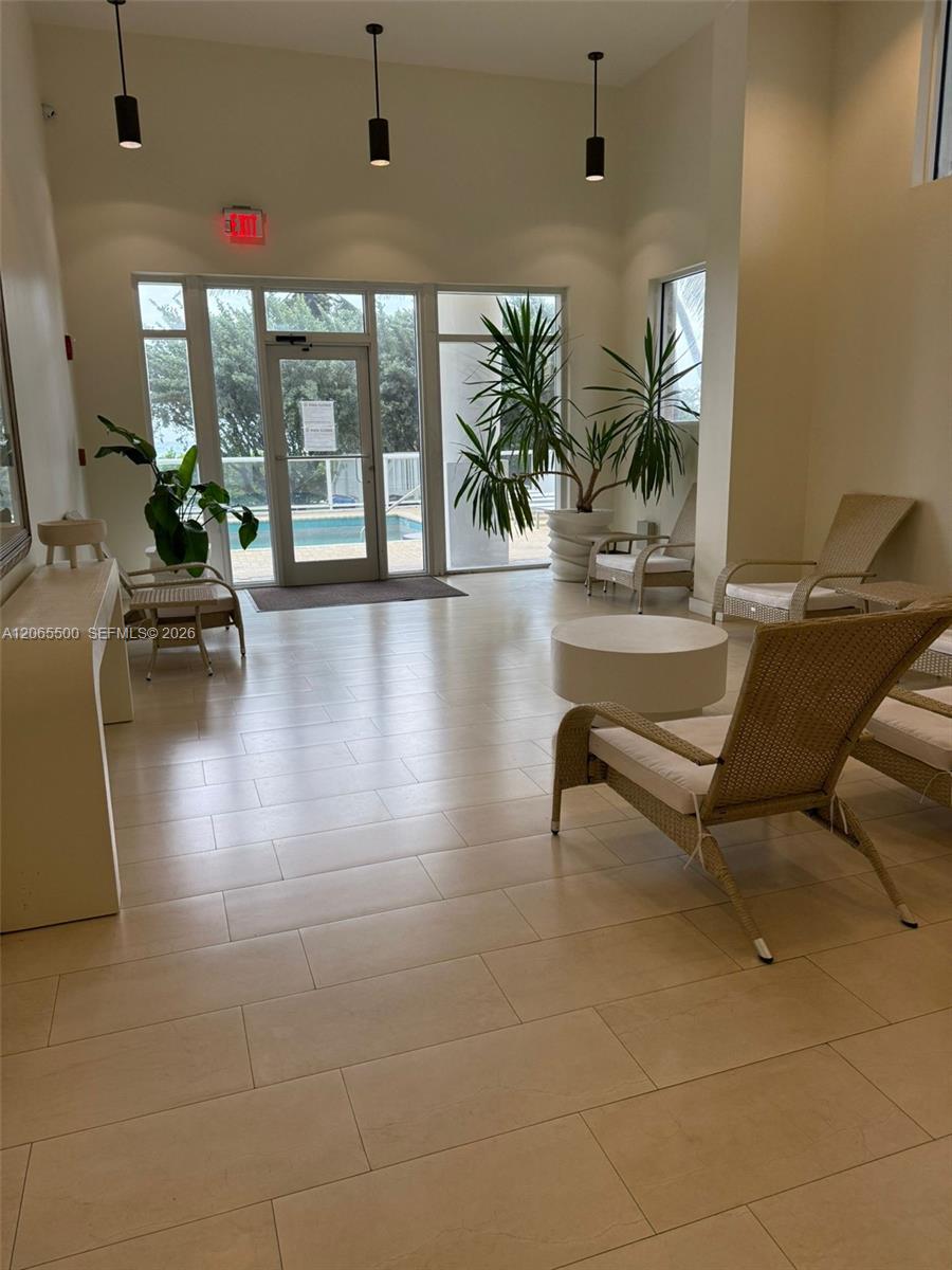 Building lounge with wicker seating and potted plants beside glass doors overlooking a pool.