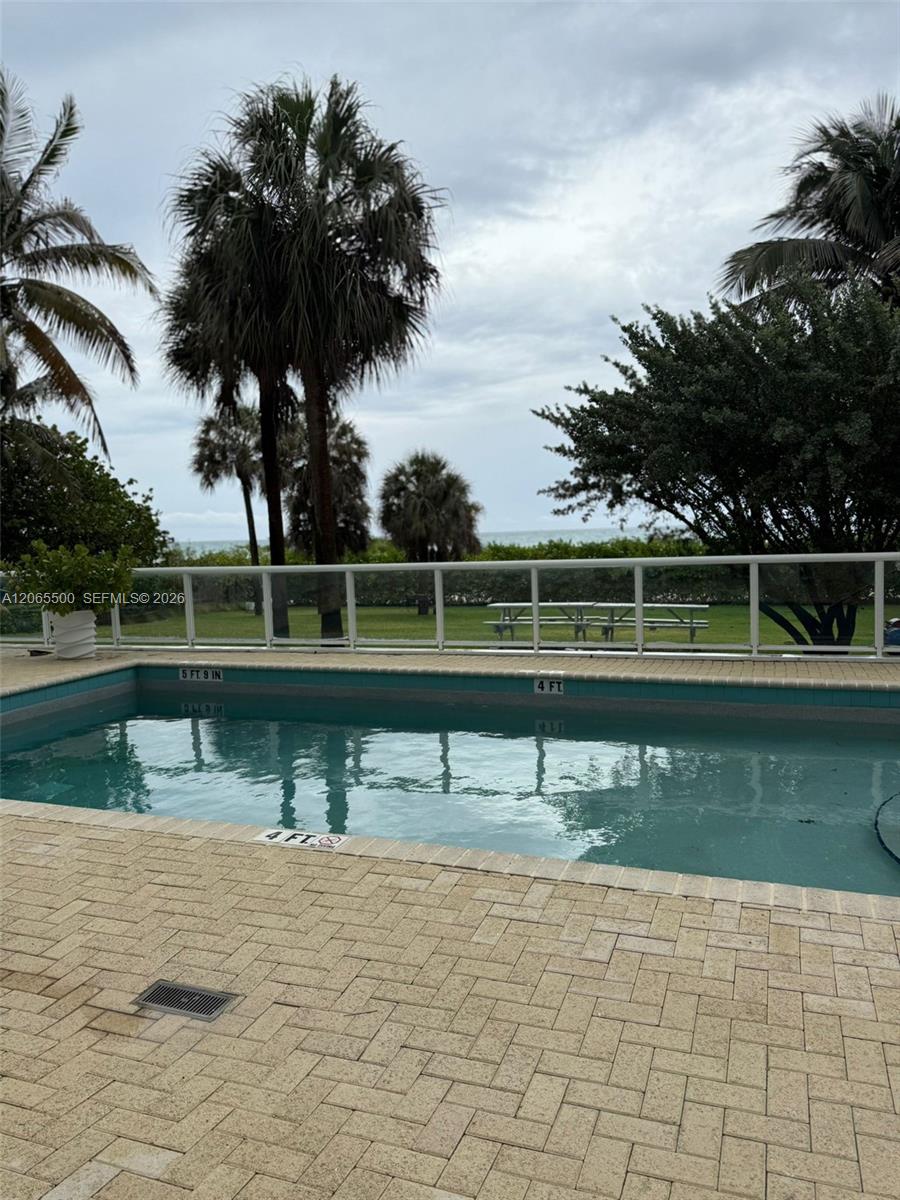 Outdoor swimming pool beside palms, with the ocean visible beyond the glass fence.
