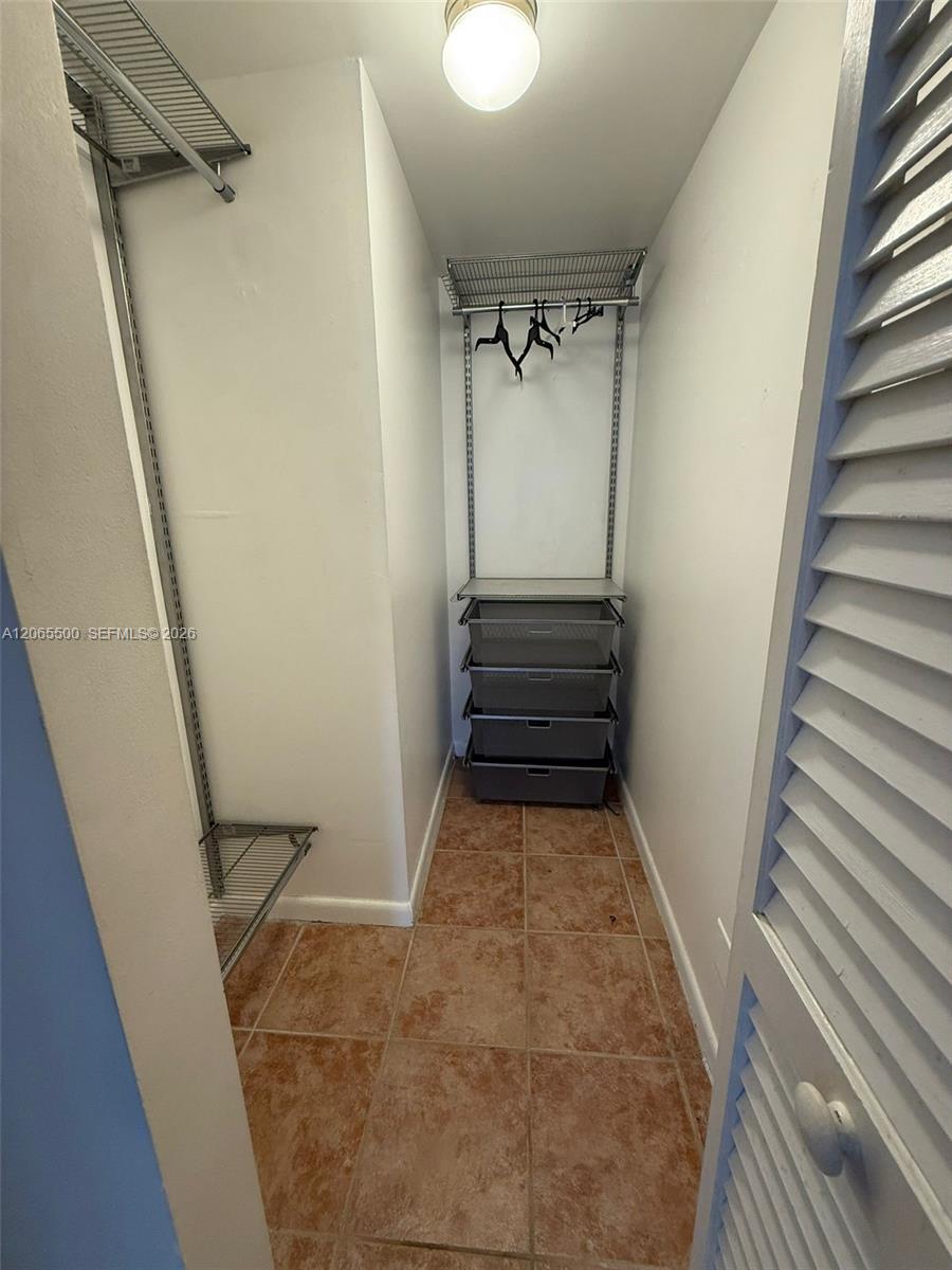 Walk-in closet with wire shelving, mesh drawers, and a brown tiled floor.