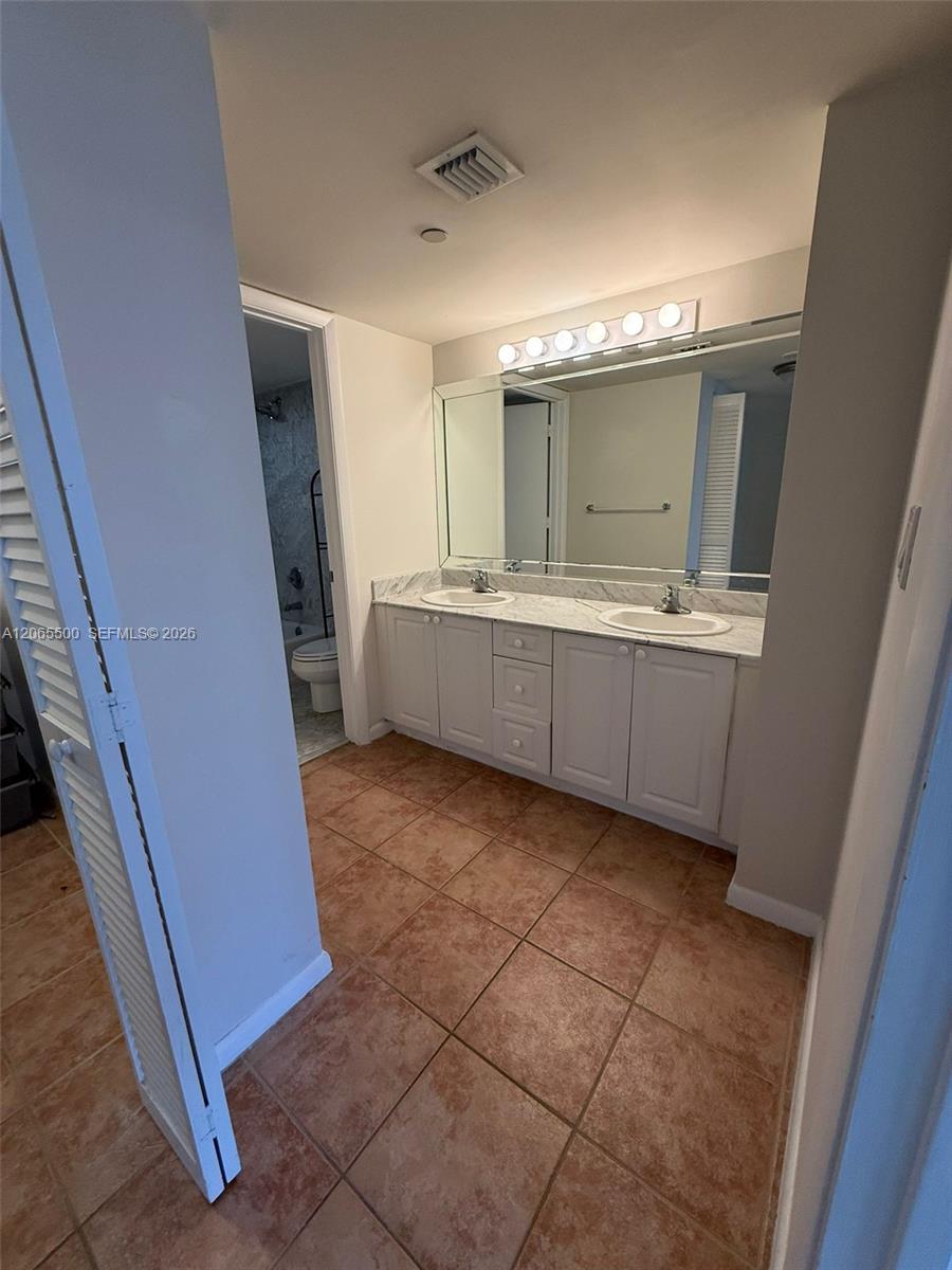 Bathroom with double vanity, large mirror, and terracotta-colored tile floor.