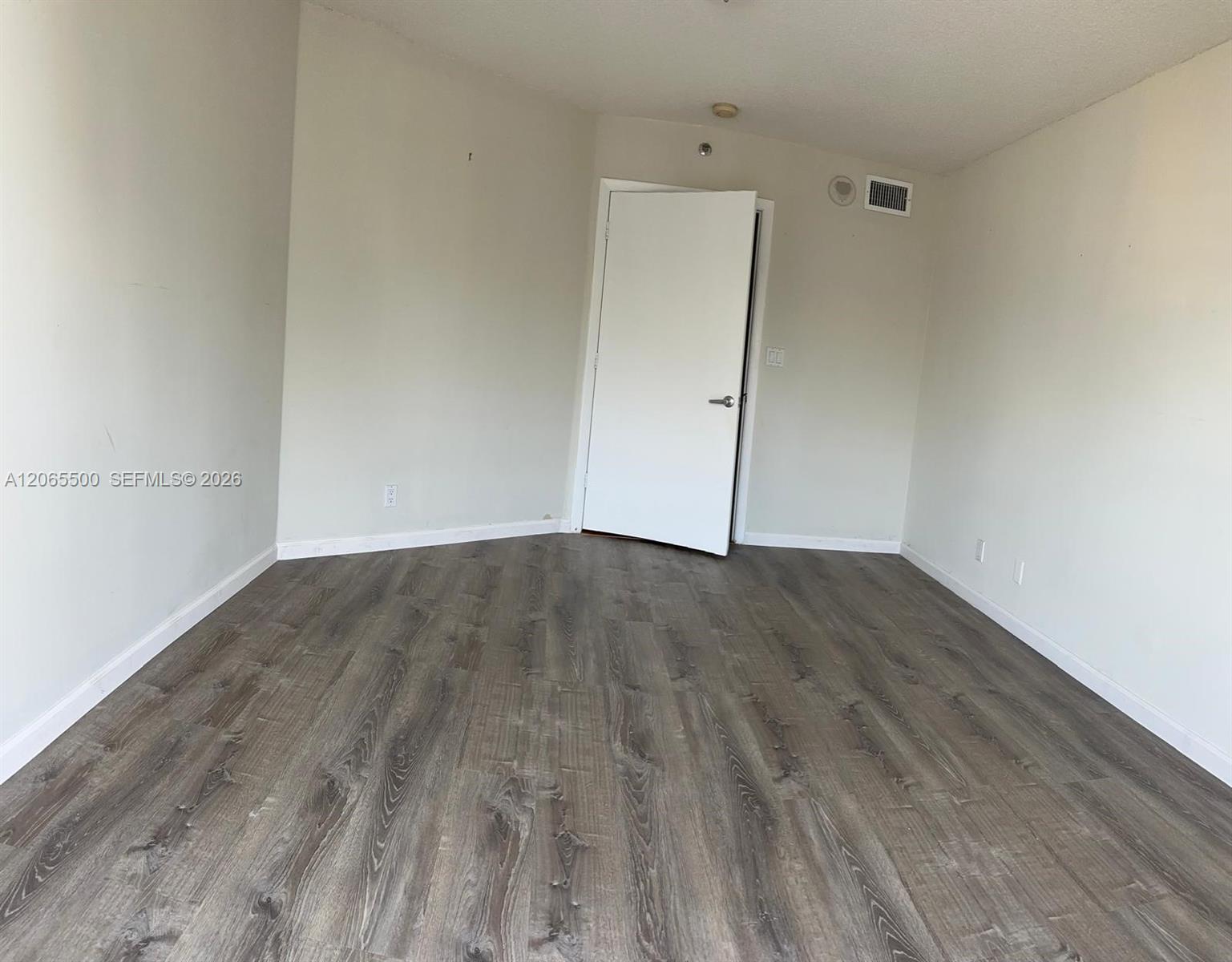 Empty room with gray-brown wood-look flooring and an open door.