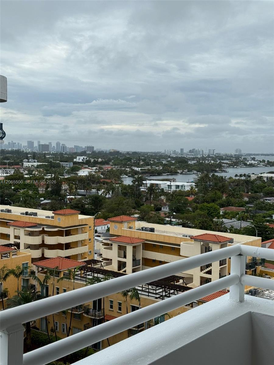 High-rise balcony view over terracotta-roofed buildings, with water and a distant skyline.