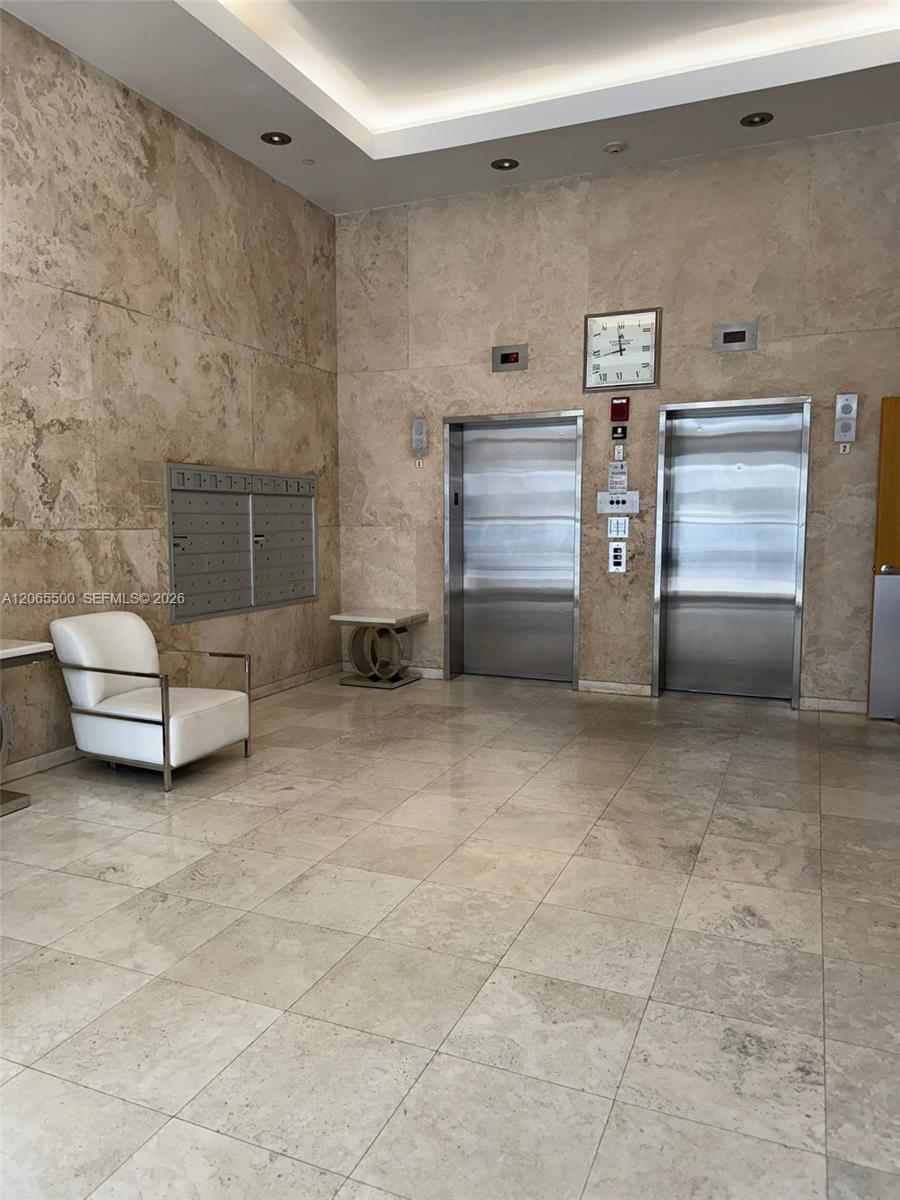 Condominium elevator lobby with two stainless-steel elevators, marble walls, mailboxes, and a white chair.