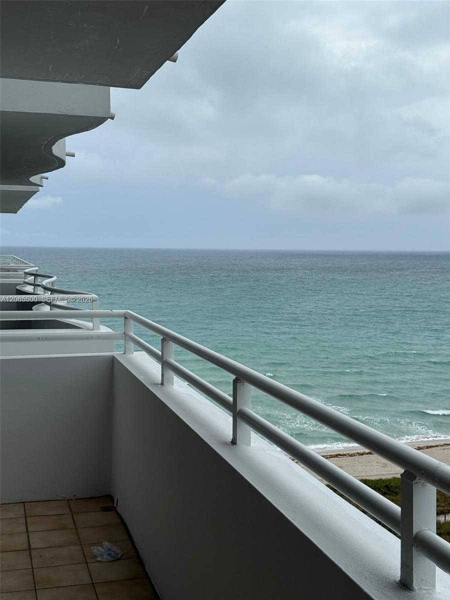 Tiled apartment balcony overlooking the ocean, with white railings and a cloudy sky.
