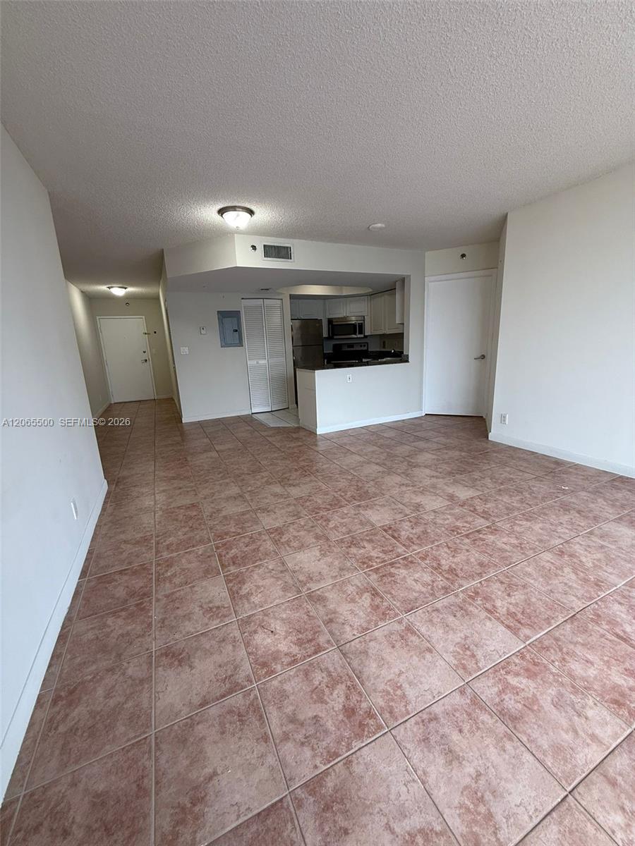 Vacant living area with reddish-brown tile floors and an open kitchen.