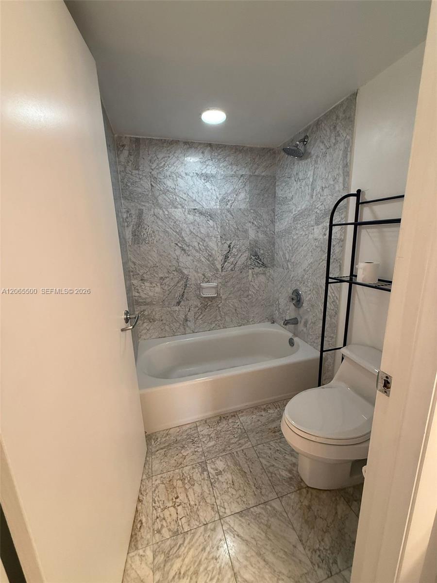 Bathroom with a white bathtub, gray marble tile, and a toilet.