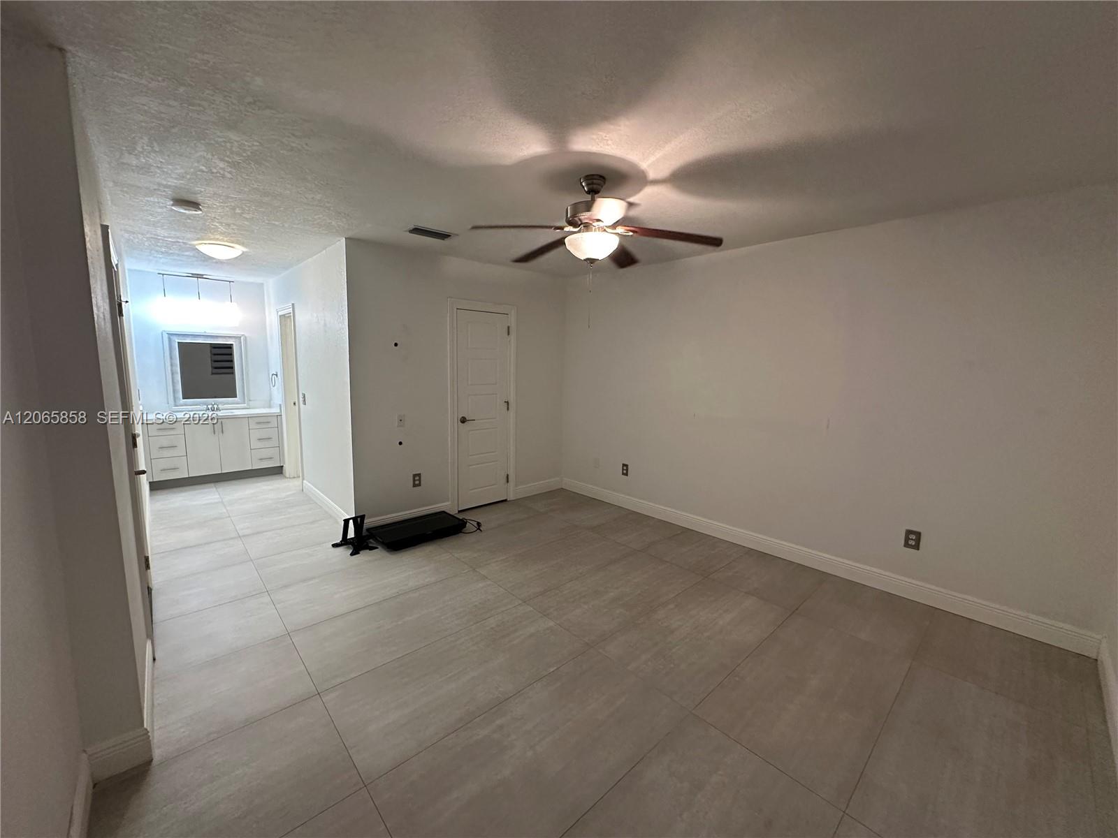 Empty tiled room with a ceiling fan and an open passage to a vanity area.