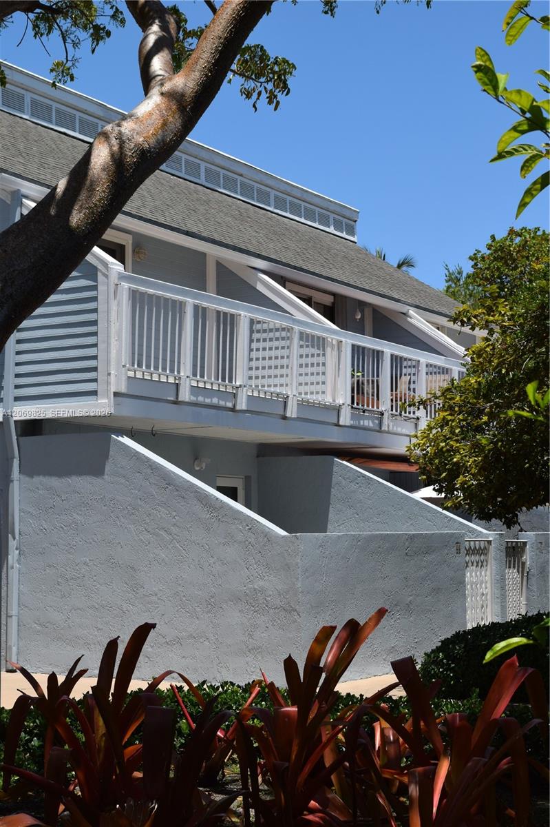 Gray residence with a long white-railed balcony, privacy walls, and tropical landscaping.
