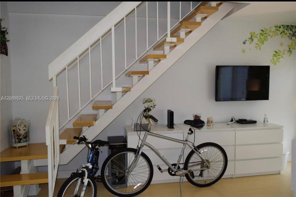 Living area with an open staircase, wall-mounted television, white media console, and two bicycles.