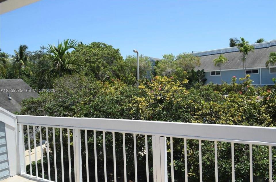 Balcony with a white railing overlooking tropical greenery and a neighboring building.