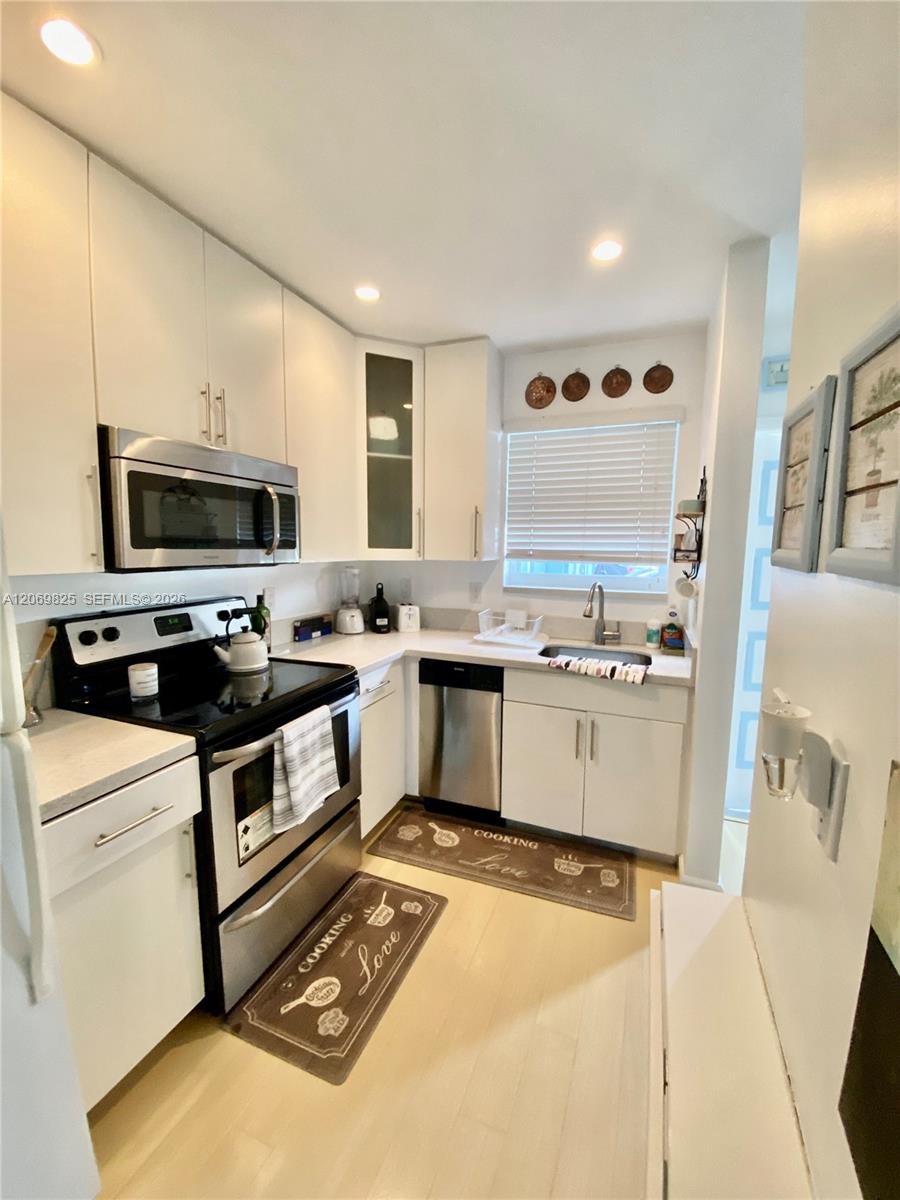 Compact kitchen with white cabinets, stainless-steel appliances, and a sink beneath a window.
