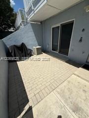 Private paved patio beside a gray stucco residence, with sliding glass doors and a low privacy wall.